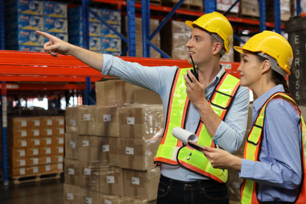 istock Group of warehouse workers with hardhats and reflective jackets using tablet, walkie talkie radio and cardboard while controlling stock and inventory in retail warehouse logistics, distribution center 1495016208