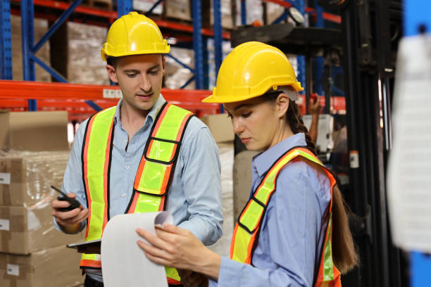 istock Group of warehouse workers with hardhats and reflective jackets using tablet, walkie talkie radio and cardboard while controlling stock and inventory in retail warehouse logistics, distribution center 1495016212