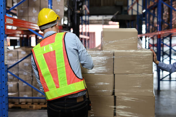 istock Rear veiw warehouse worker man with hardhat and reflective jackets wrapping boxes in stretch film parcel on pallet while control stock and inventory in retail warehouse logistics distribution center 1495016339