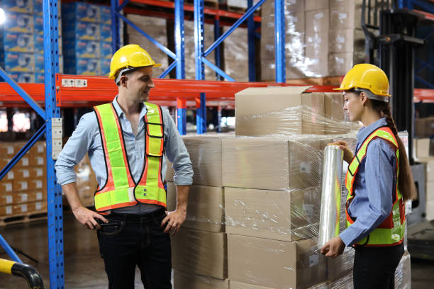 istock Group of warehouse workers with hardhats and reflective jackets using tablet, walkie talkie radio and cardboard while controlling stock and inventory in retail warehouse logistics, distribution center 1495016353