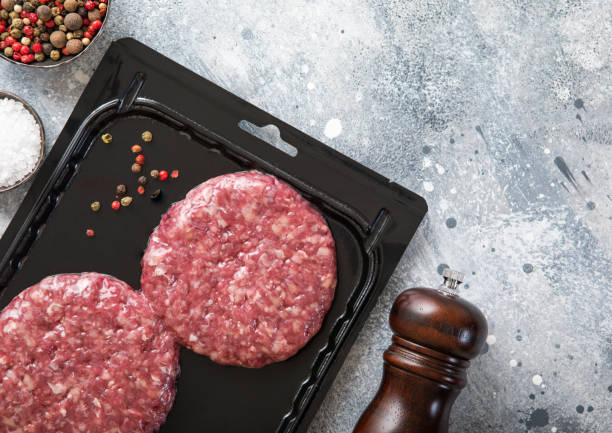 istock Beef fresh raw organic burgers in vacuum tray with pepper grinder on light kitchen table background. 1495019050