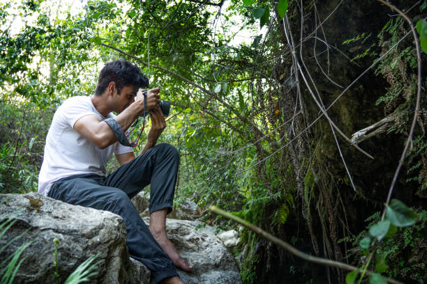 istock Young man sitting on rock and photographing in forest during vacation 1495021285