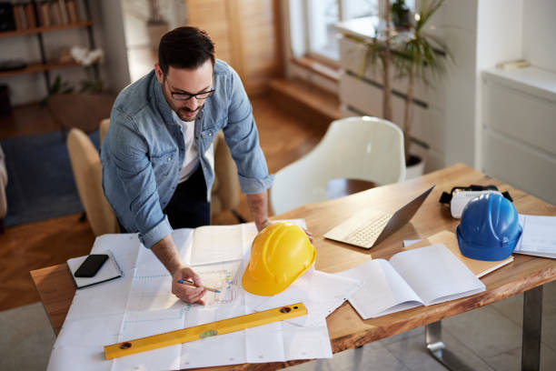 istock Above view of young building contractor analyzing plans while working at home office. 1495022605