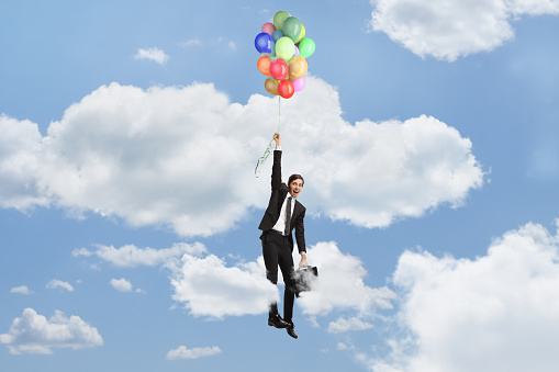 Businessman holding balloons and flying up in the sky