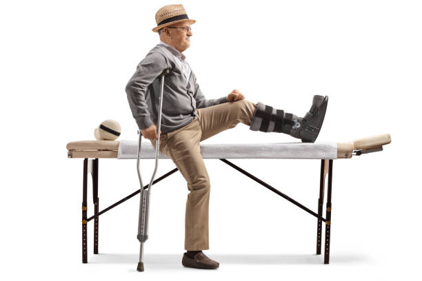 elderly male patient sitting on a physical therapy bed with a brace on his leg - physical injury men orthopedic equipment isolated on white imagens e fotografias de stock