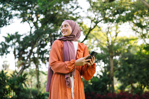Portrait of Asian Malay female holding phone in a public park.