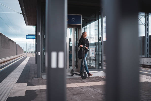istock sustainable public transport - woman with e-scooter at platform 1495025957