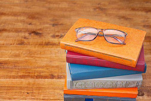 Stack of books with eyeglasses on wooden background. Education concept