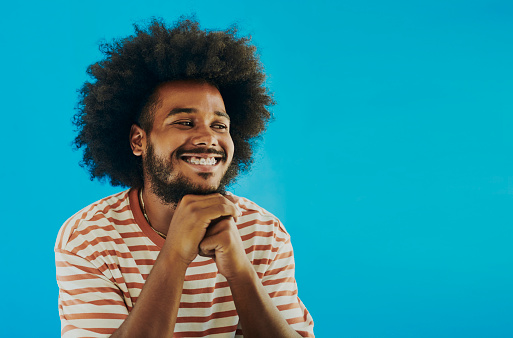 Image of a smiling, young black man with dental braces and an afro hairstyle and beard looking to the side. Shot against a blue background. Stock photo