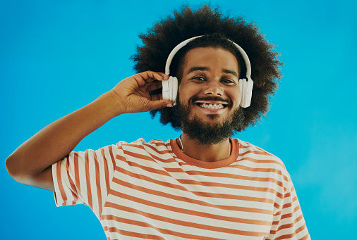 Young black man with an afro hairstyle and beard listening to music while holding headphones and looking into the camera, Stock image