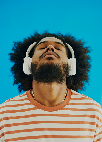 Head shot of a young black man standing and bending his head backwards whilst listening to music through his headphones. Stock photo