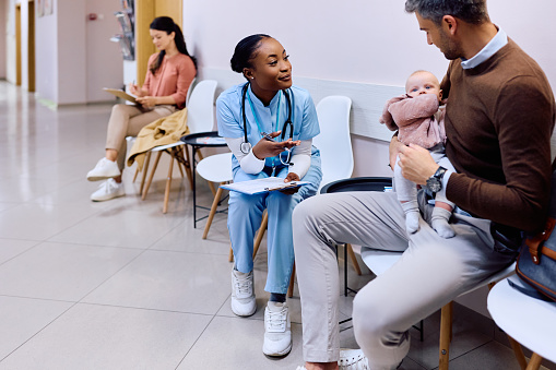 Black pediatric nurse communicating with father who brought with baby daughter to the clinic.