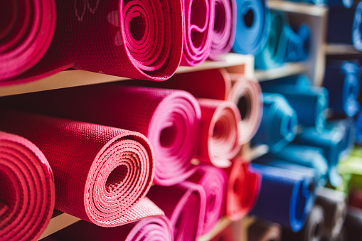 Focus on pink colored yoga mats lying rolled up on shelves by other mats in different colors in exercising facility