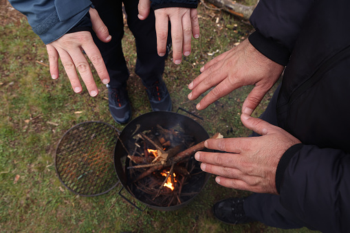 Close-up on hand of men warming on campfire.