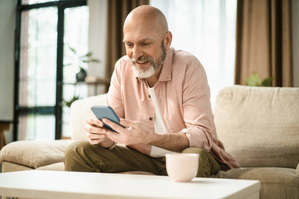 istock Happy mid aged man text message on phone while sit on sofa in home interior. 1495030890
