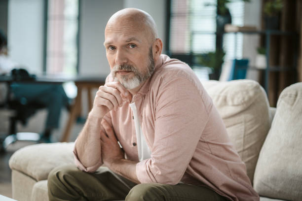 istock Wise senior man, with touch of grey in beard, looks directly into camera within cozy interior of home. His hand gently rests upon silver beard, exuding sense of thoughtfulness and contemplation. 1495031004