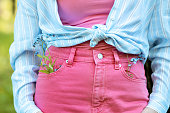Young lady in pink skinny jeans and blue shirt. Blue fowers in pants pocket. White striped shirt and stylish jeans.