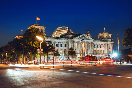 the illuminated  Berlin Reichstag at night with lights of cars in the foreground