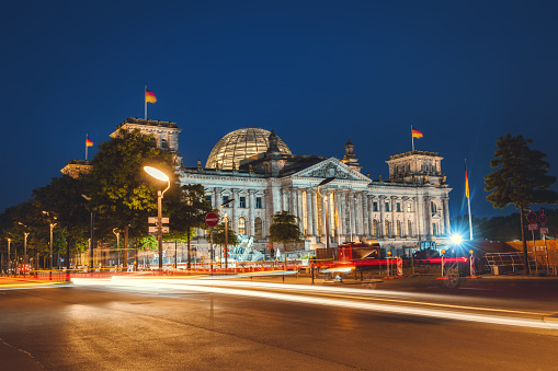 the illuminated  Berlin Reichstag at night with lights of cars in the foreground