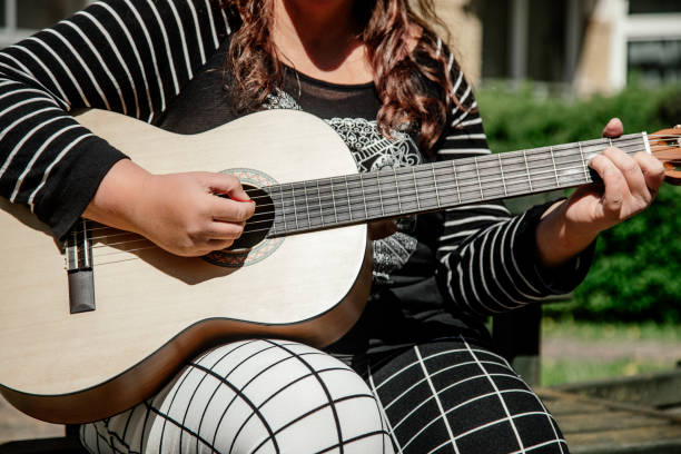 une personne méconnaissable est une femme en pull à manches longues jouant de la guitare, assise sur un banc sur la place de la ville. - musical instrument nature outdoors musician photos et images de collection