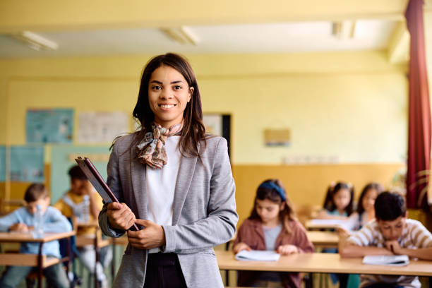 istock Happy elementary school teacher in the classroom looking at camera. 1495037844
