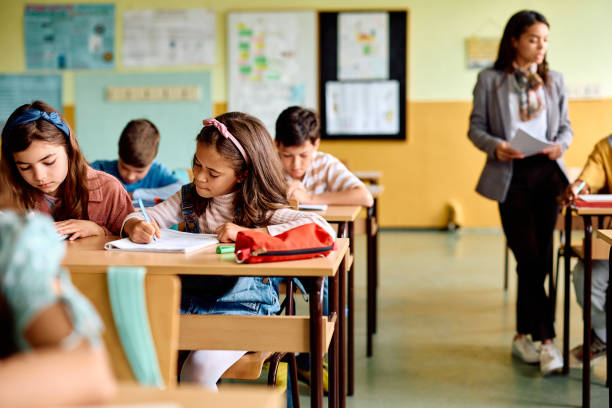 istock Hispanic schoolgirl and her classmates writing in the classroom. 1495037881