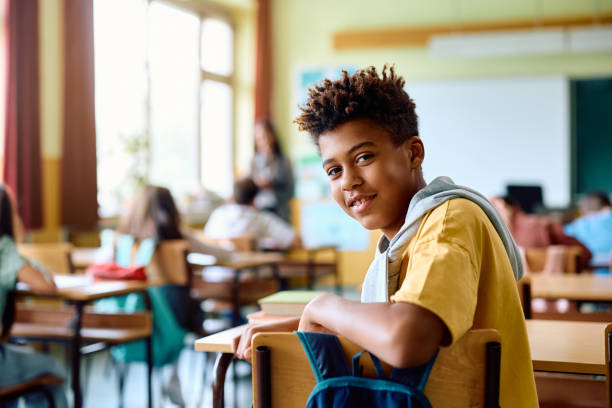 istock Happy black schoolboy having a class in the classroom and looking at camera. 1495037942