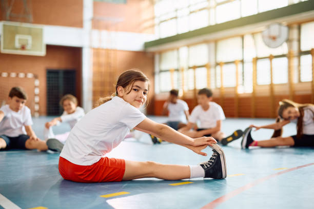 istock Smiling schoolgirl stretching her leg during physical activity class and looking at camera. 1495037972
