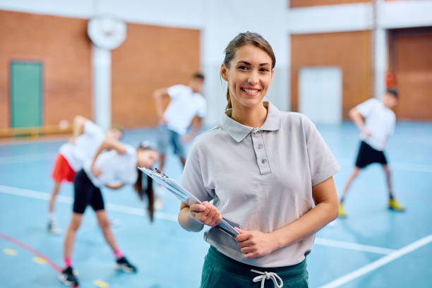 istock Happy sports teacher looking at camera during PE class with elementary students at school gym. 1495037991