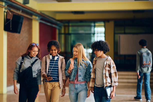 istock Group of high school friends using cell phone while walking through hallway. 1495038077