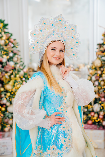 portrait of Snow Maiden in a blue traditional costume with a kokoshnik in a room with christmas tree. The concept of Russian New Year's traditions. Congratulations to children.
