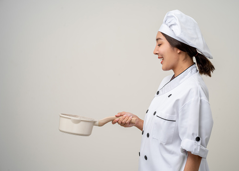 Young beautiful asian woman chef in uniform holding soup pot ladle utensils cooking in the kitchen various gesture menu good taste on isolated. Cooking woman chef people in kitchen restaurant