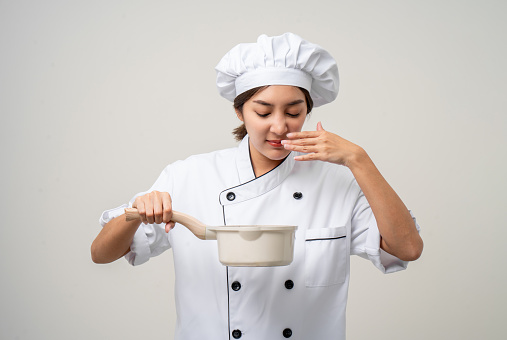 Bad smell and not tasty food. Young asian woman chef in uniform holding soup pot ladle utensils cooking in the kitchen various gesture  on isolated. Cooking woman chef people in kitchen restaurant