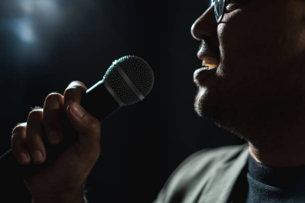 istock Confident successful speaker man talking on stage with spotlight strike through the darkness at corporate business event. Public speaker giving talk at conference hall. Stand up comedian. 1495043130