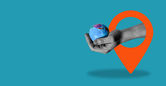 A digital collage of contemporary art. Hand-holding globe with navigation icon, blue background with space for text.