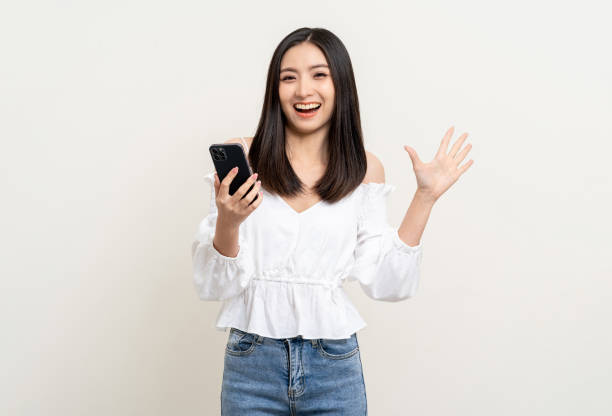 istock Pretty young asian woman using smartphone standing on isolated white background. Excited Beautiful young asian shopping online payment with mobile phone. Playing game on smartphone 1495043557