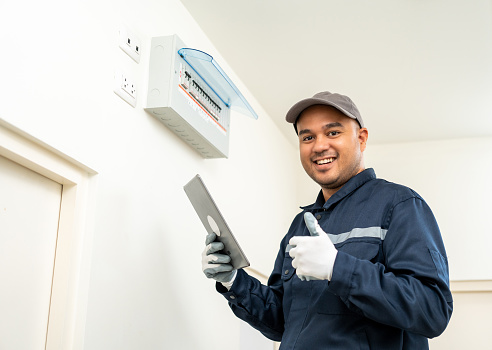 Electrician man in uniform using tablet for maintenance or fixing switches sockets  circuit breaker electrical system. Technician fixing an electric fuse at home. Home service concept.