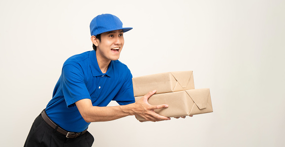 Asian man in blue uniform standing holding box parcel cardboard and smartphone on isolated white background. Male service worker with cell phone. Delivery courier shipping service