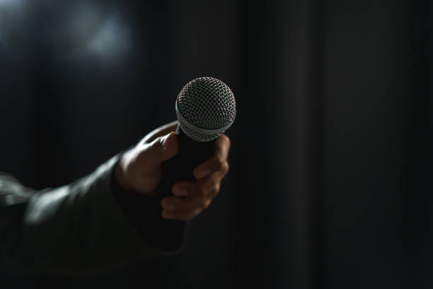 istock Confident successful speaker man talking on stage with spotlight strike through the darkness at corporate business event. Public speaker giving talk at conference hall. Stand up comedian. 1495045103