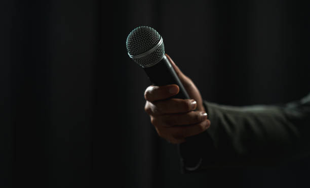 istock Confident successful speaker man talking on stage with spotlight strike through the darkness at corporate business event. Public speaker giving talk at conference hall. Stand up comedian. 1495045452