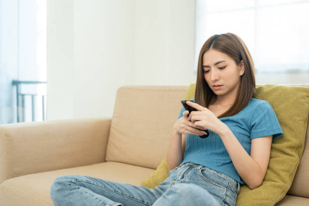 istock Asian woman watching television using remote to change choose the program menu. Sitting in living room relaxing on the couch. 1495046778