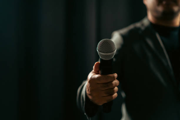 istock Confident successful speaker man talking on stage with spotlight strike through the darkness at corporate business event. Public speaker giving talk at conference hall. Stand up comedian. 1495046848