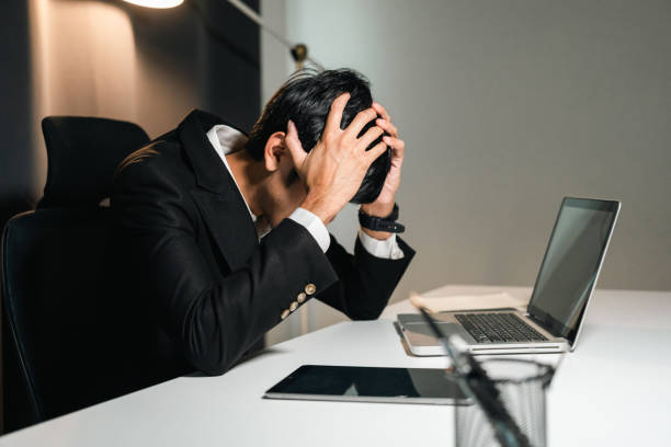 istock Asian businessman working with laptop computer in the dark office at night. Indian man work hard overtime serious thinking hand on head. Feeling stressed and headache in warm light late at night 1495046905