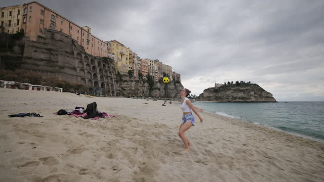 Mother and teenage kids playing with ball on a beach in Tropea