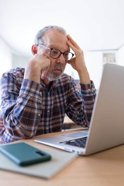 istock Stressed and disappointed senior caucasian man using laptop at home feeling overwhelmed. Vertical image. 1495047626