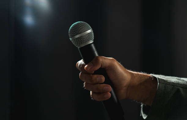 istock Confident successful speaker man talking on stage with spotlight strike through the darkness at corporate business event. Public speaker giving talk at conference hall. Stand up comedian. 1495048109