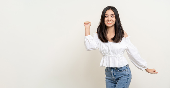 Cheerful cute asian female teenager listen to the music and dancing on isolated white background. Happy Beautiful pretty young woman in white shirt having fun with the music in room.