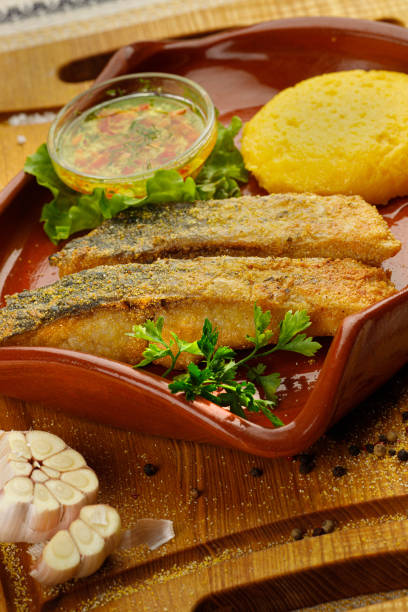 grilled fish pieces with mamaliga, closeup Whole fried fish in a red plate served with mamaliga and garlic souce mamaliga stock pictures, royalty-free photos & images