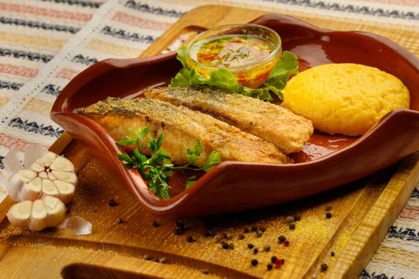 grilled fish pieces with mamaliga, closeup Whole fried fish in a red plate served with mamaliga and garlic souce mamaliga stock pictures, royalty-free photos & images