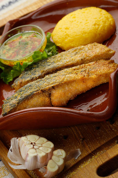 grilled fish pieces with mamaliga, closeup Whole fried fish in a red plate served with mamaliga and garlic souce mamaliga stock pictures, royalty-free photos & images